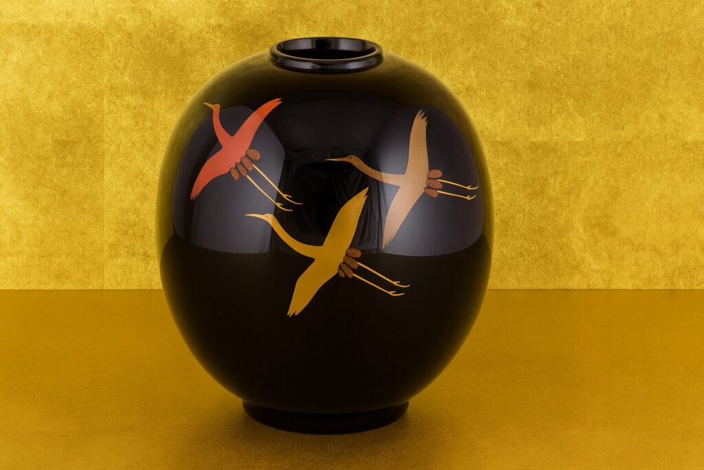 Black lacquer vase with gold and red flying crane design on a golden background