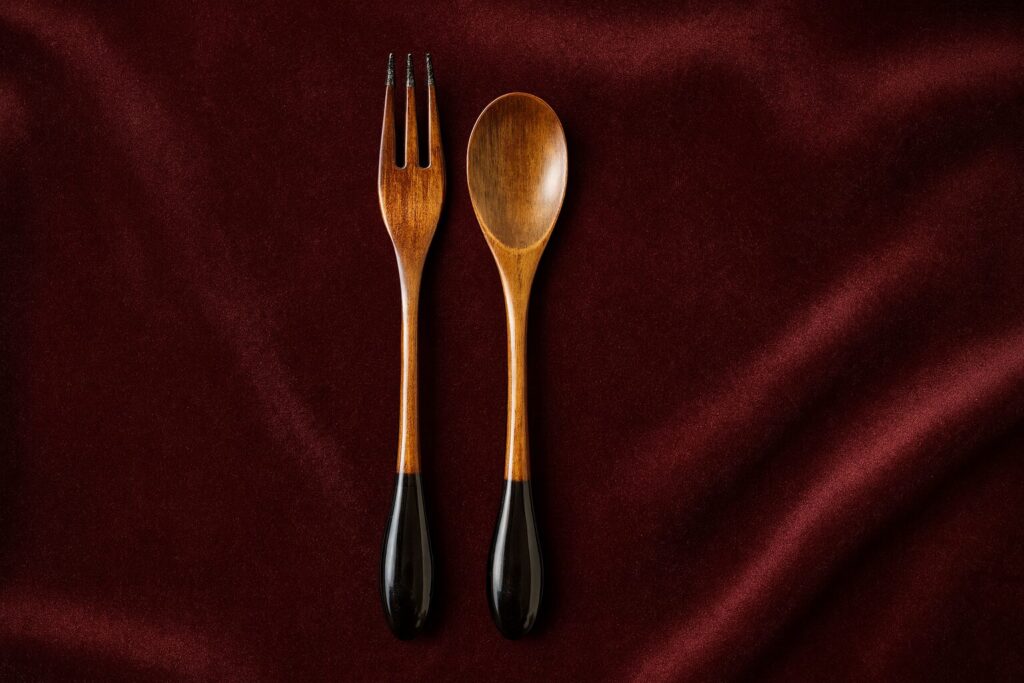 Wooden fork and spoon set with sleek black lacquered handles on burgundy fabric background