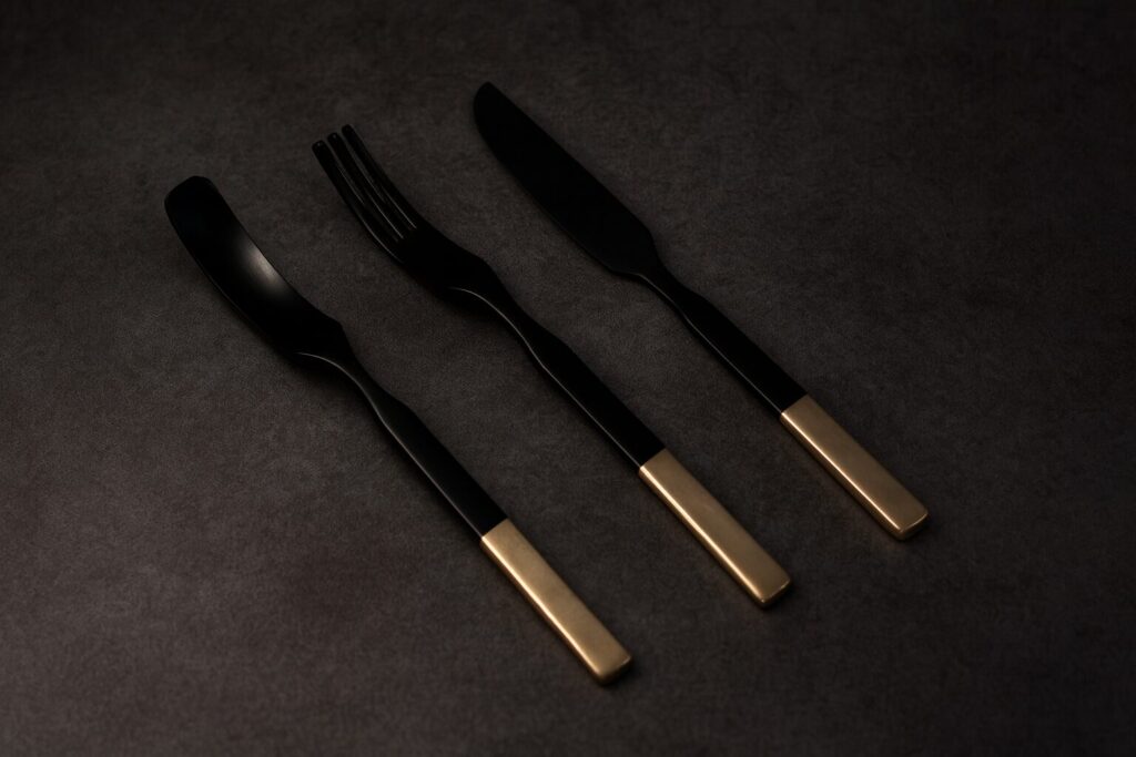 Elegant black lacquer spoon, fork, and knife set with gold handles on dark textured background