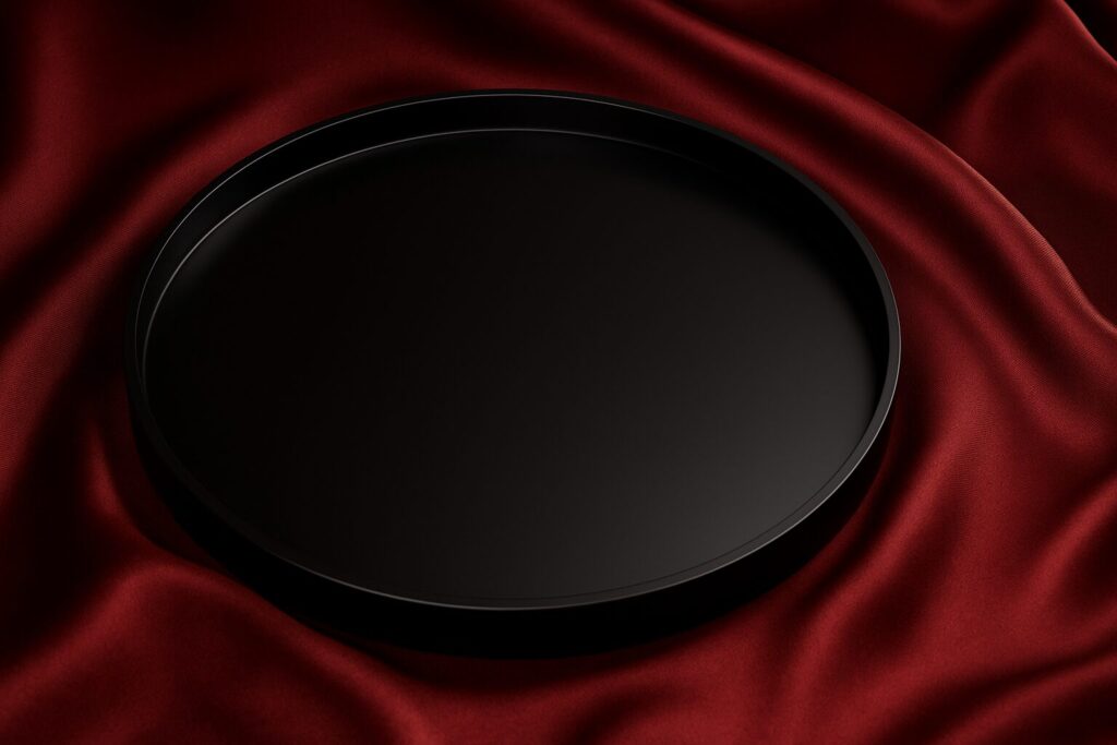 Minimalist round black lacquer tray displayed on rich red silk fabric background