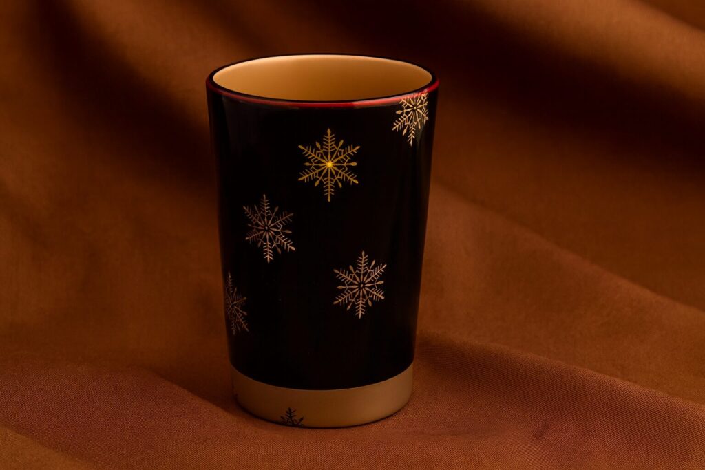 Black ceramic cup with golden snowflake pattern on a warm brown fabric background