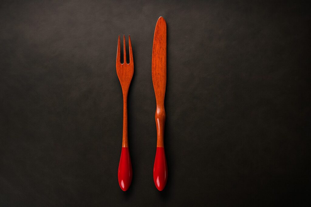 Handcrafted wooden fork and knife set with glossy red lacquered handles on dark leather background