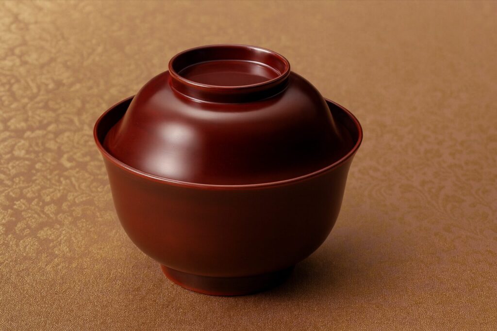 Matte brown lacquer Japanese soup bowl with lid, displayed on a gold-patterned fabric background