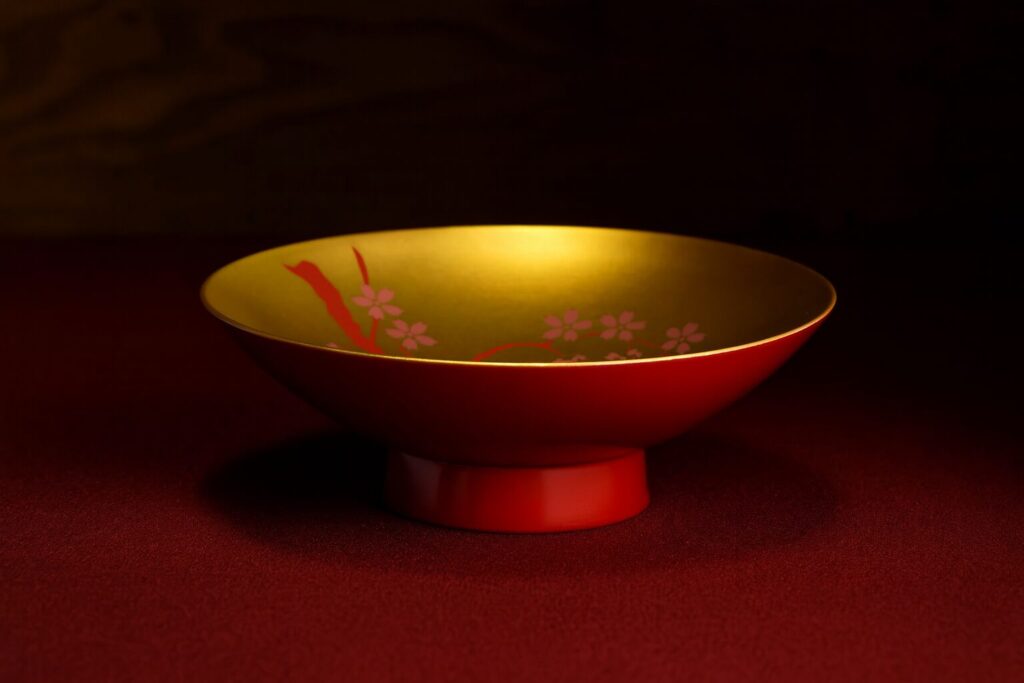 Red lacquer bowl with gold interior and pink cherry blossom design on a deep red surface
